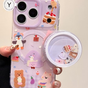 May include: A lavender phone case with a clear, round, liquid-filled compartment. The case features various cartoon food and animal designs, including a penguin, bear, and cake. The text "Y2CASE" and "OWOCASE" are visible.