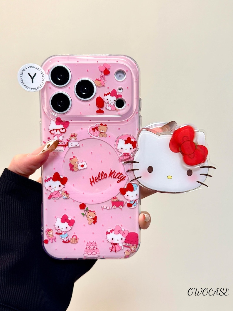 Pu&ograve; includere: Custodia per telefono rosa con personaggi di Hello Kitty e la scritta "Hello Kitty". La custodia ha un bordo trasparente e un ciondolo 3D di Hello Kitty. Il design include fiocchi, orsi e torte. La custodia &egrave; progettata per un telefono.