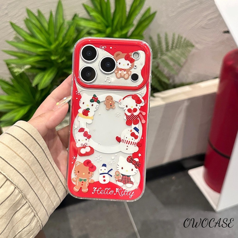 May include: Red and clear phone case featuring Hello Kitty characters in festive holiday attire. The case has a red border and a clear center, with the words "Hello Kitty" printed on the bottom. The case is designed for a smartphone.