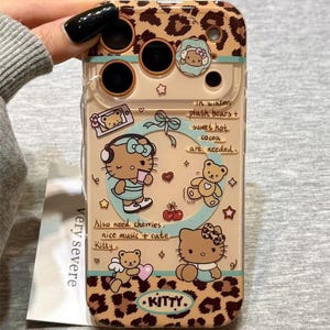 May include: A clear phone case with a leopard print design and illustrations of Hello Kitty and teddy bears. The case features text that reads "In winter, plush bears + sweet hot cocoa are needed." and "Also need cherries, nice music + cute Kitty."