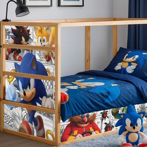 Op de afbeelding: Een houten bedframe met een blauwe Sonic the Hedgehog-thema beddengoedset. Het bed heeft een blauw dekbed, kussen en een pluche Sonic-speelgoed. Het bedframe heeft panelen in stripstijl met Sonic en andere personages.
