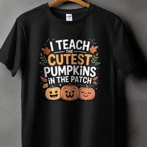 May include: Black t-shirt with the text "I teach the cutest pumpkins in the patch" in white and orange. The design includes three smiling pumpkin faces and fall leaves, perfect for Halloween or a teacher.