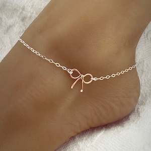May include: A silver chain anklet with a rose gold bow charm.