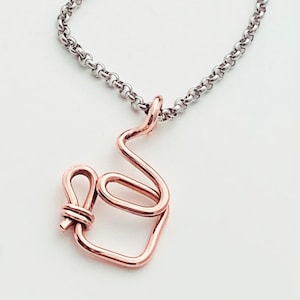 May include: A rose gold necklace with a delicate, abstract pendant made of twisted wire. The pendant is shaped like a stylized letter 'S' with a small loop at the bottom. The necklace is made of a silver chain.