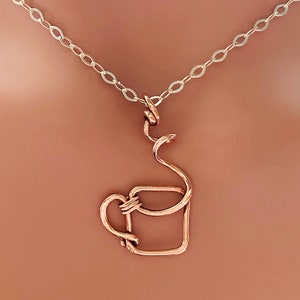 May include: A copper-colored wire pendant necklace featuring a coffee cup design. The cup is square with a curved handle and a swirling steam detail. The necklace has a silver chain.