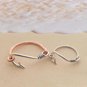 May include: Two silver and copper hook-shaped rings. The ring on the left is copper with a silver hook. The ring on the right is silver with a silver hook.