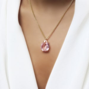 Könnte beinhalten: Eine zarte goldene Kettenkette mit einem birnenförmigen Anhänger aus rosa Edelstein.