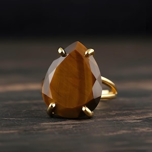 A large, oval-shaped amber-colored gemstone, possibly a diamond or amber, is displayed on a gold ring against a dark background.