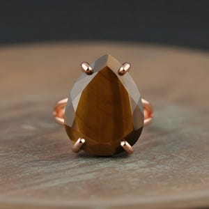 A large, brown gemstone ring with a teardrop shape sits on a wooden surface.