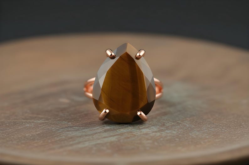 A large, brown gemstone ring with a teardrop shape sits on a wooden surface.