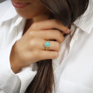 May include: A gold ring featuring a turquoise gemstone surrounded by smaller clear stones.