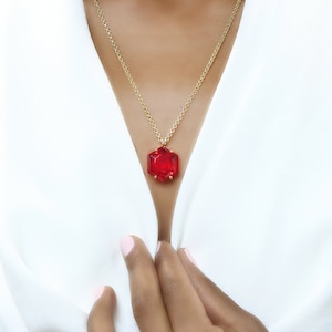 May include: A gold chain necklace with a large, red, faceted gemstone pendant.