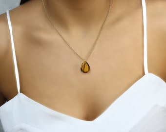 Op de afbeelding: Een gouden ketting met een traanvormige hanger van tijgeroog.