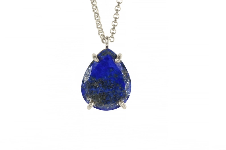 May include: A silver chain necklace with a teardrop-shaped lapis lazuli pendant. The pendant is set in silver and has a dark blue color with gold flecks.