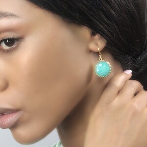 May include: A pair of gold earrings with a turquoise gemstone. The earrings have a delicate, intricate design.