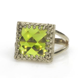 Puede incluir: Un anillo de plata con una gran piedra preciosa cuadrada verde engastada en un marco decorativo.