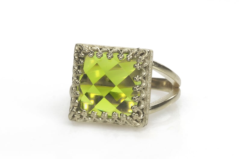 Puede incluir: Un anillo de plata con una gran piedra preciosa cuadrada verde engastada en un marco decorativo.