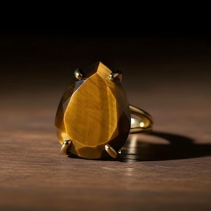 A large, yellow gemstone ring with a pointed top sits on a wooden surface, casting a shadow.