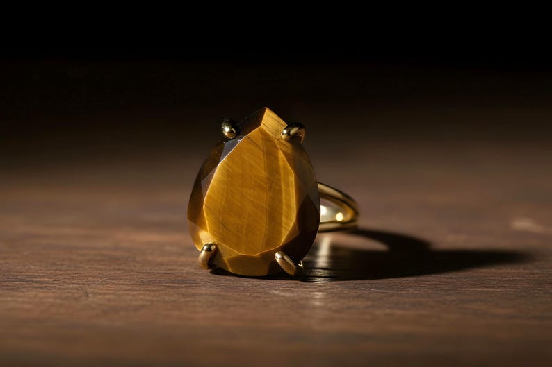 A large, yellow gemstone ring with a pointed top sits on a wooden surface, casting a shadow.