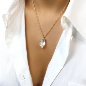 May include: A gold chain necklace with a clear crystal pendant. The pendant is shaped like a marquise and has a gold setting.