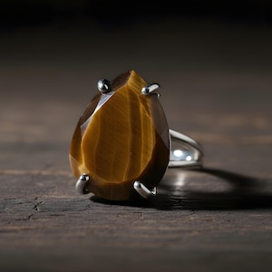 A close-up image of a large, oval-shaped amber-colored gemstone, possibly a diamond or amber, set in a silver ring.