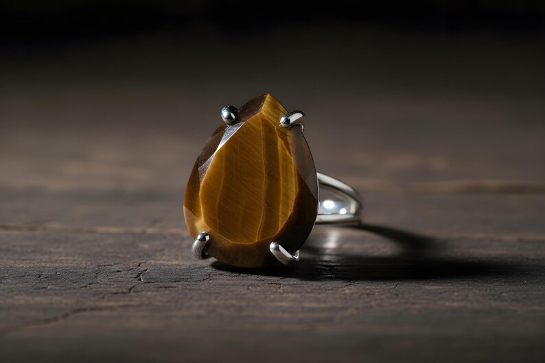 A close-up image of a large, oval-shaped amber-colored gemstone, possibly a diamond or amber, set in a silver ring.