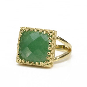 Puede incluir: Anillo dorado con una piedra preciosa verde cuadrada y facetada. La piedra preciosa est&aacute; engastada en un marco decorativo calado. El anillo tiene un dise&ntilde;o de ca&ntilde;a dividida.