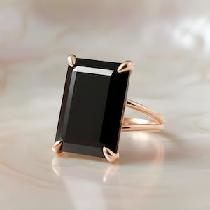 Puede incluir: Un anillo de oro rosa con una gran piedra negra rectangular. El anillo tiene un dise&ntilde;o de ca&ntilde;a dividida y cuatro garras que aseguran la piedra. El engaste y la banda tienen un acabado pulido, sobre un fondo neutro.