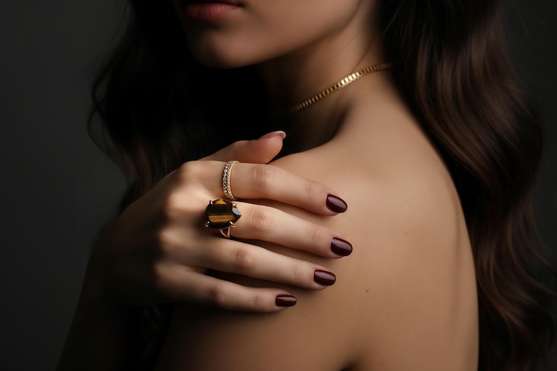 A close-up of a woman's hand wearing a ring and nail polish, with long dark hair.