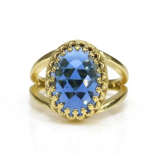 K&ouml;nnte beinhalten: Ein goldener Ring mit einem blauen, ovalen Edelstein, der in einem dekorativen Goldrahmen gefasst ist.