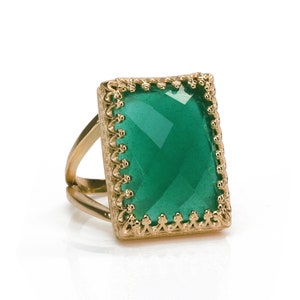 以下が含まれることがあります： 装飾的な枠にセットされた大きな正方形の緑色の宝石が付いた金の指輪