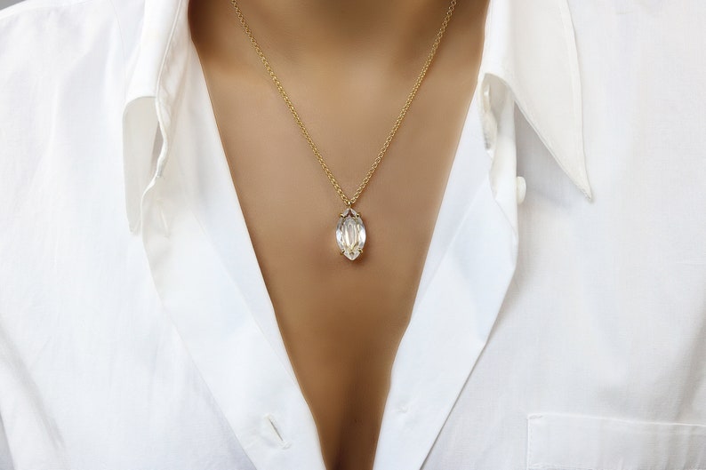May include: A gold chain necklace with a clear, faceted, marquise-shaped pendant.