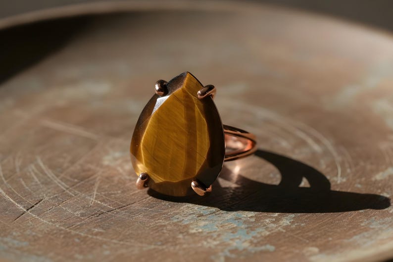 A large, irregularly shaped amber-colored gemstone, possibly a diamond or amber, is displayed on a metal ring against a textured background.
