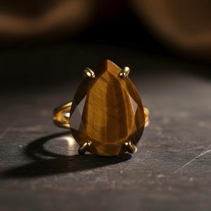 A close-up image of a gold ring with a large, irregularly shaped gemstone, likely a diamond, set in the center of the ring.