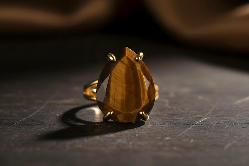 A close-up image of a gold ring with a large, irregularly shaped gemstone, likely a diamond, set in the center of the ring.