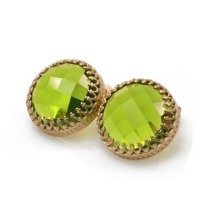May include: A pair of green gemstone earrings with gold settings. The earrings have a round, faceted design and are set in a delicate, ornate frame.