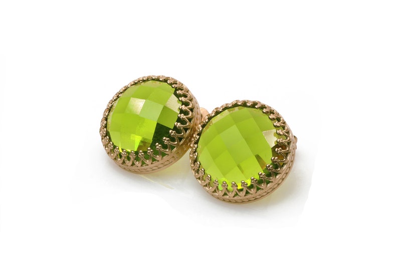 May include: A pair of green gemstone earrings with gold settings. The earrings have a round, faceted design and are set in a delicate, ornate frame.
