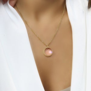 Op de afbeelding: Een gouden ketting met een ronde hanger met een lichtroze edelsteen omringd door een gouden parelrand.