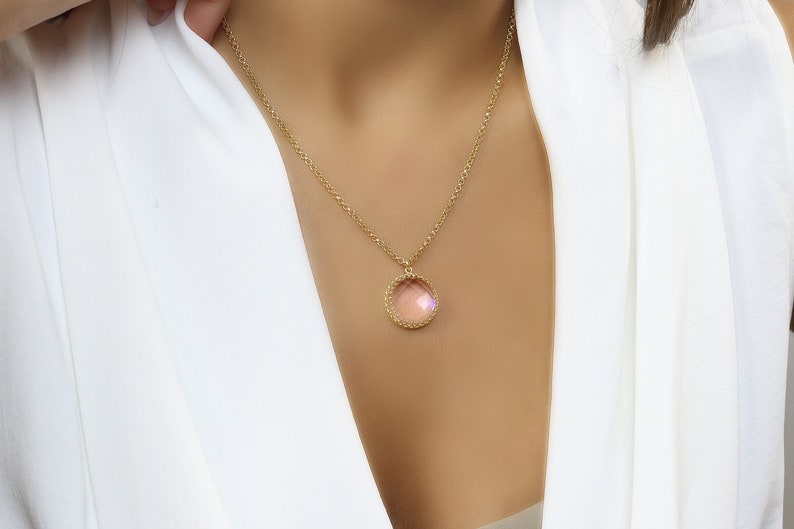 Op de afbeelding: Een gouden ketting met een ronde hanger met een lichtroze edelsteen omringd door een gouden parelrand.