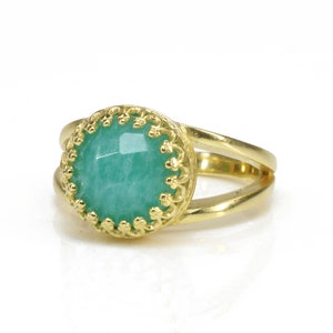 May include: A gold ring featuring a green gemstone set within an ornate gold bezel. The ring has a double band design.