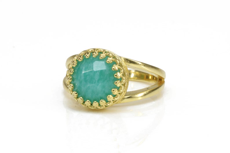 May include: A gold ring featuring a green gemstone set within an ornate gold bezel. The ring has a double band design.