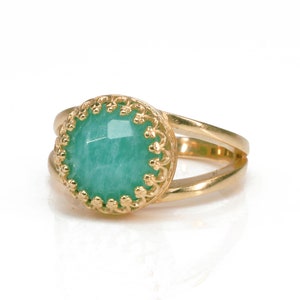 May include: A gold ring featuring a green gemstone set within an ornate gold bezel. The ring has a double band design.