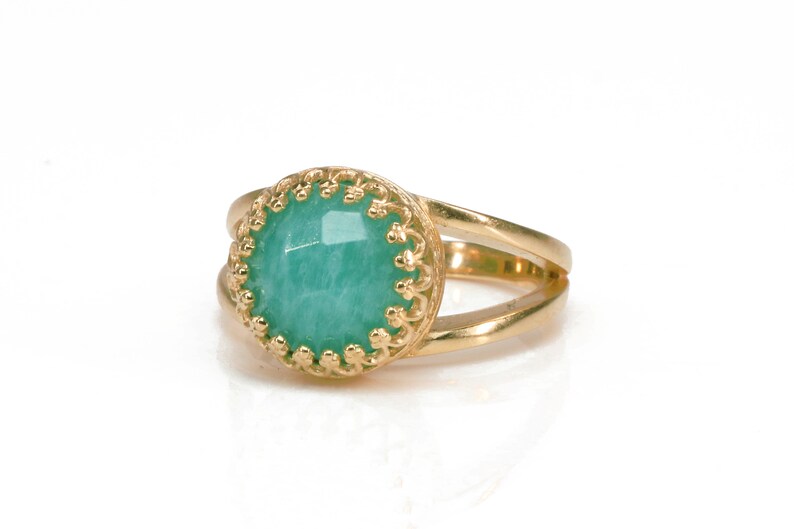 May include: A gold ring featuring a green gemstone set within an ornate gold bezel. The ring has a double band design.