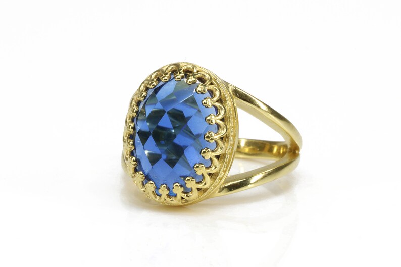 K&ouml;nnte beinhalten: Ein goldener Ring mit einem gro&szlig;en, facettierten blauen Edelstein, der in einer verzierten goldenen Fassung sitzt.