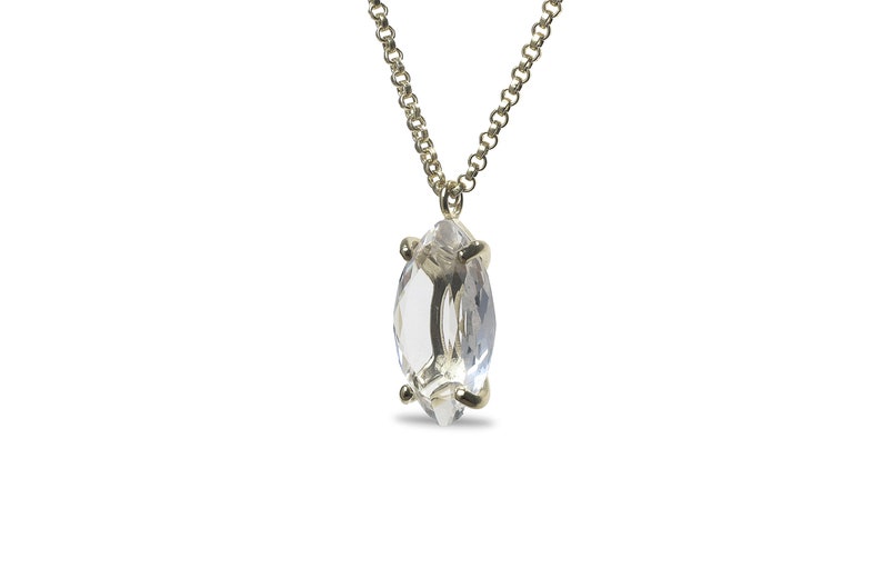 May include: A delicate gold chain necklace with a clear marquise-shaped crystal pendant.