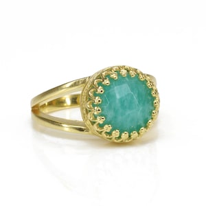 May include: A gold ring with a green gemstone set in a decorative gold bezel. The ring has a double band.