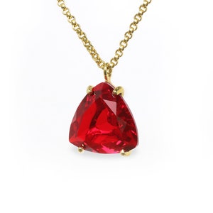 May include: A gold chain necklace with a large, red, triangular gemstone pendant.