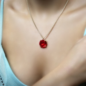 May include: A gold chain necklace with a large, red, oval-shaped gemstone pendant.
