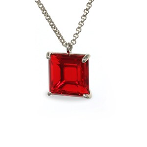 May include: A silver chain necklace with a red square-shaped gemstone pendant.