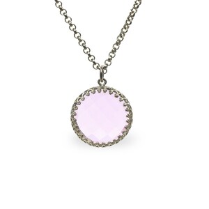 Op de afbeelding: Een zilveren ketting met een ronde hanger met een lichtroze edelsteen omgeven door een zilveren filigraanontwerp.